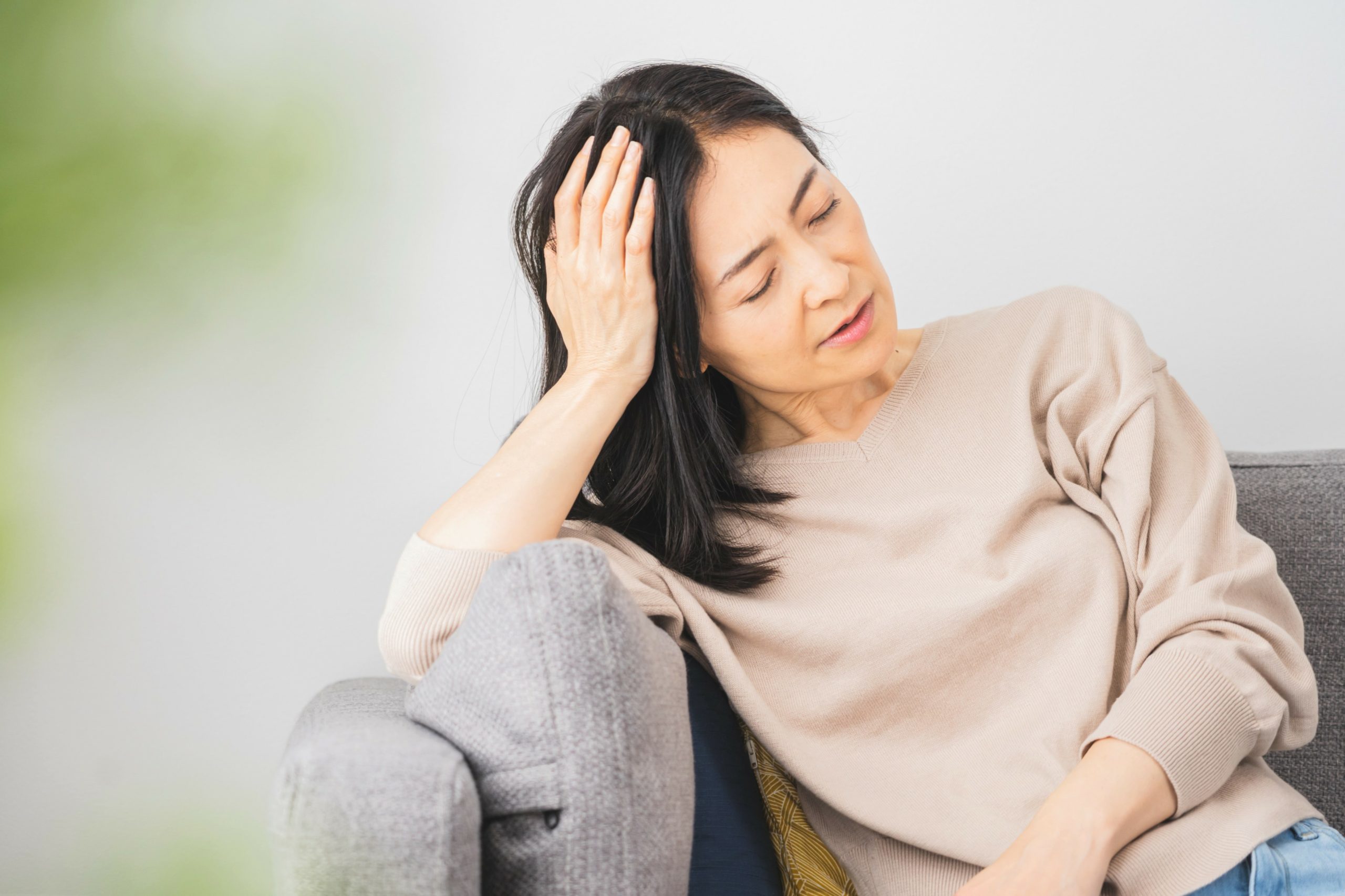 woman in her 40s sitting on a couch holding her head