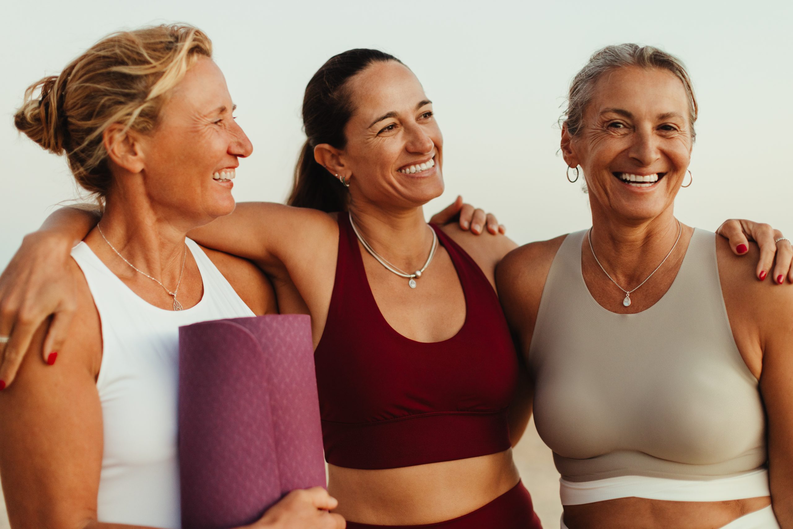 Three smiling women in athletic wear standing together.