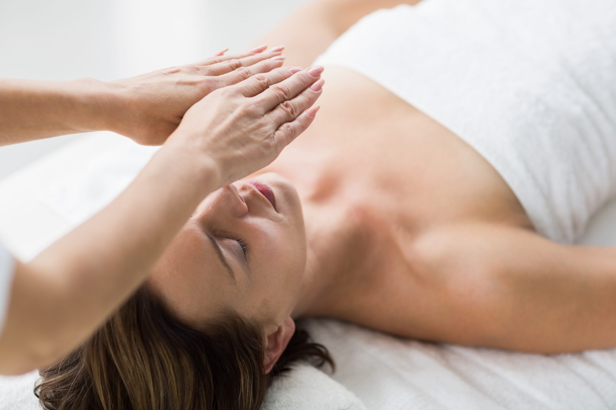 Practitioner holding both hands above a relaxed woman’s forehead during a therapeutic energy healing session.