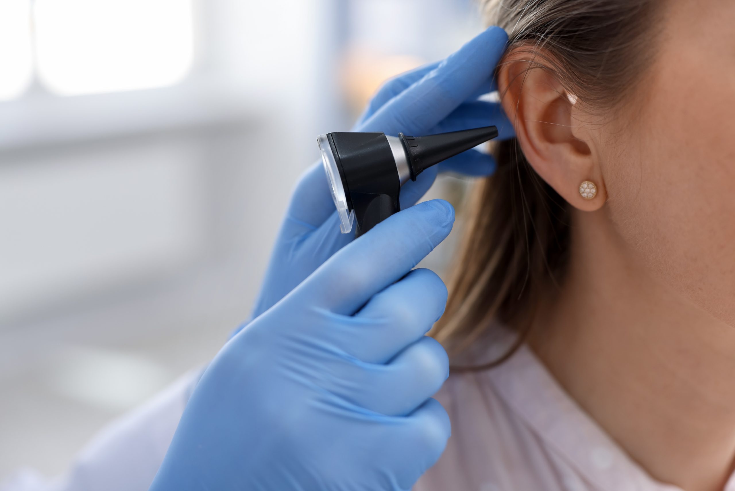 Healthcare professional using an otoscope to examine a woman’s ear canal.