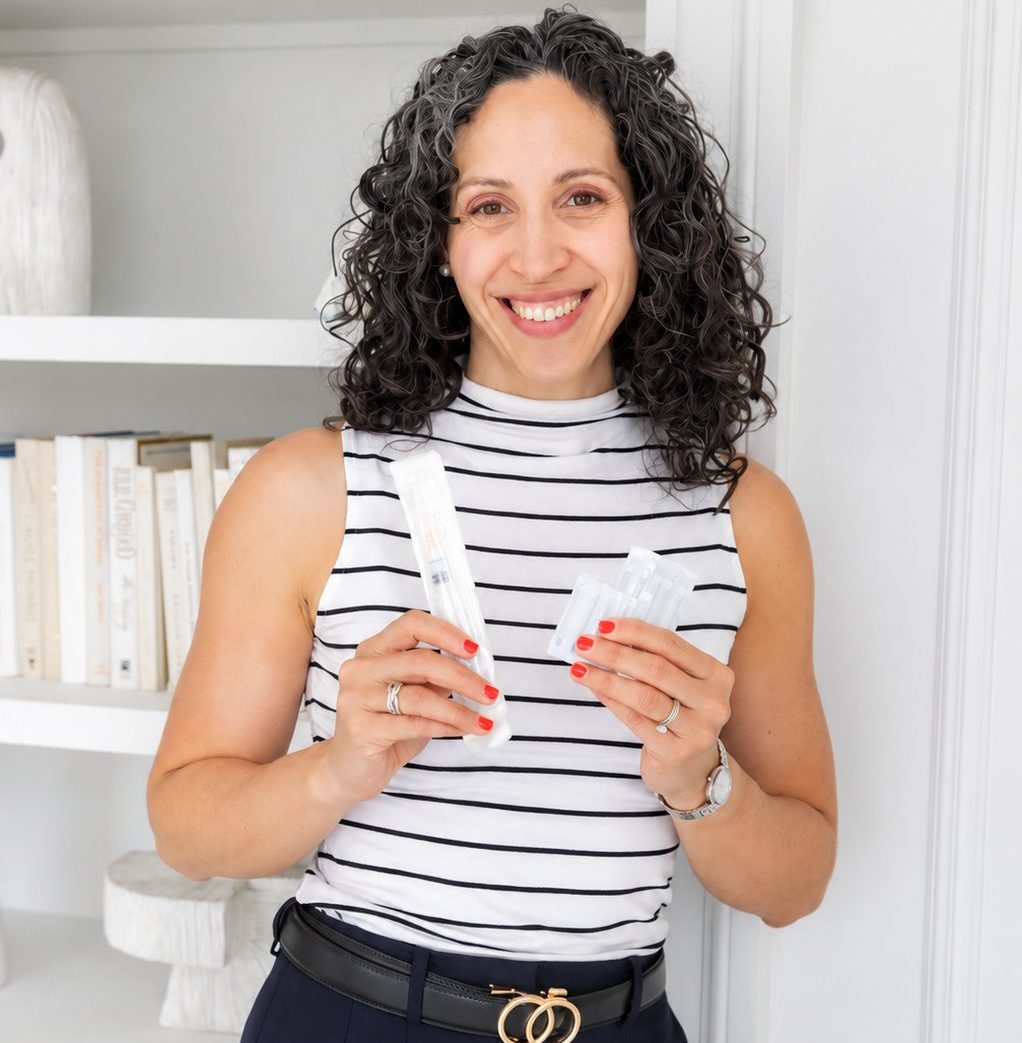 Dr. Lisa smiles while holding packaged syringes used for B12 injections.
