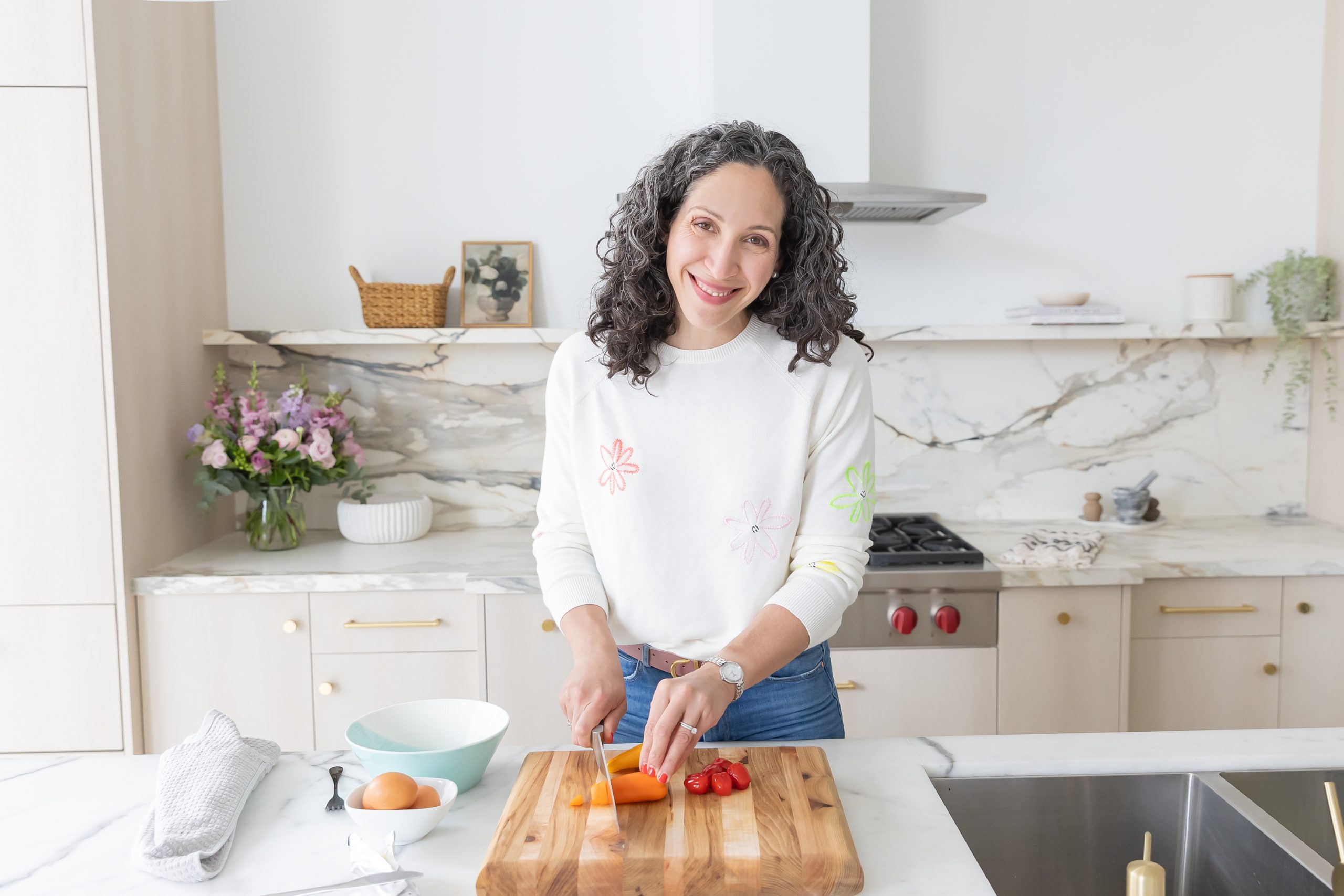 Dr. Lisa smiles while mixing ingredients in a bowl beside fresh vegetables and eggs.