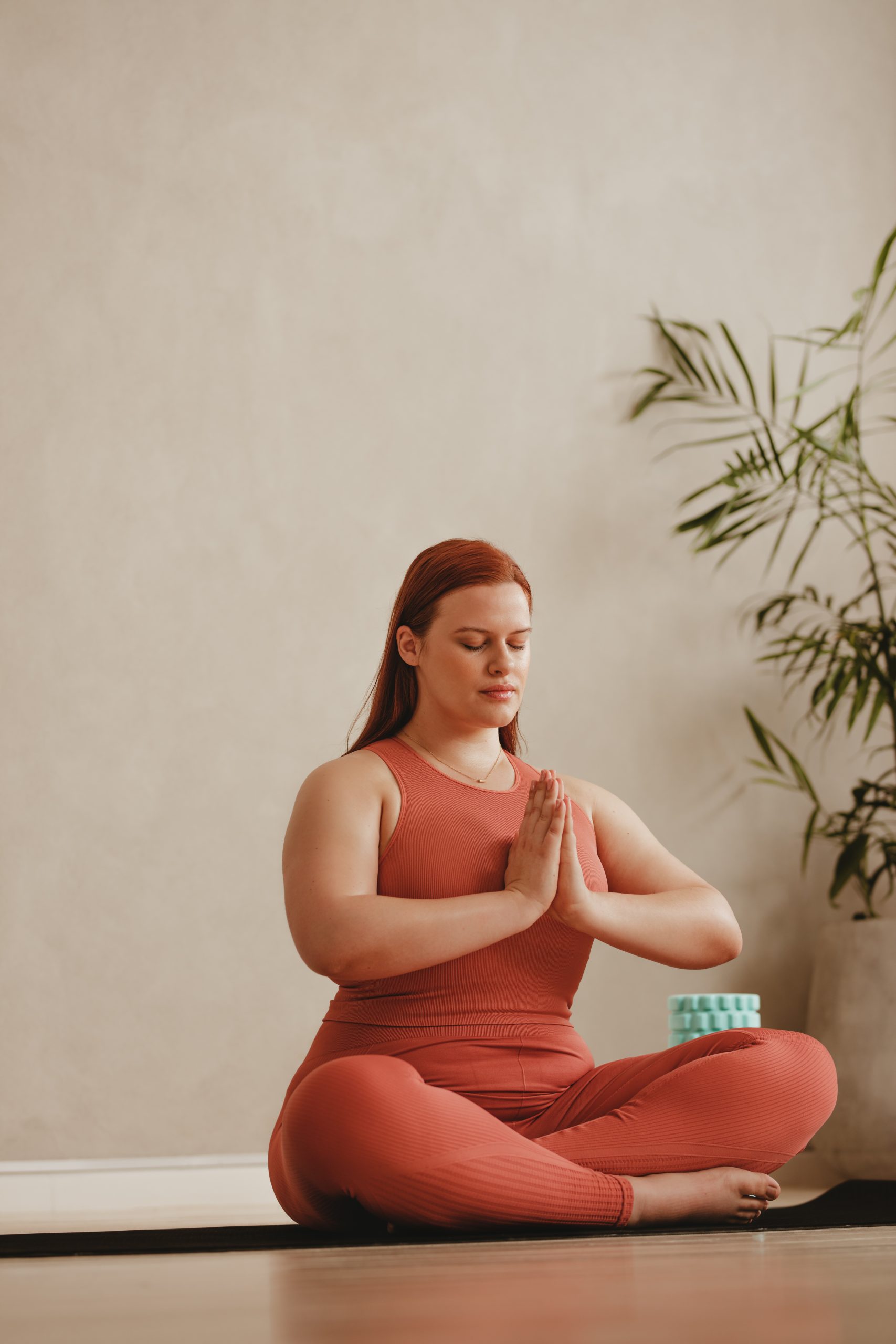 Woman seated cross-legged on a yoga mat, meditating with her hands in prayer position.